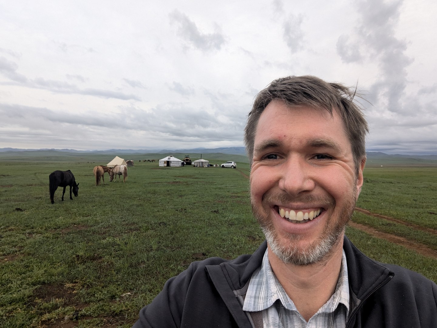 Edward smiling in the Mongolian countryside, with horses and yurts behind him